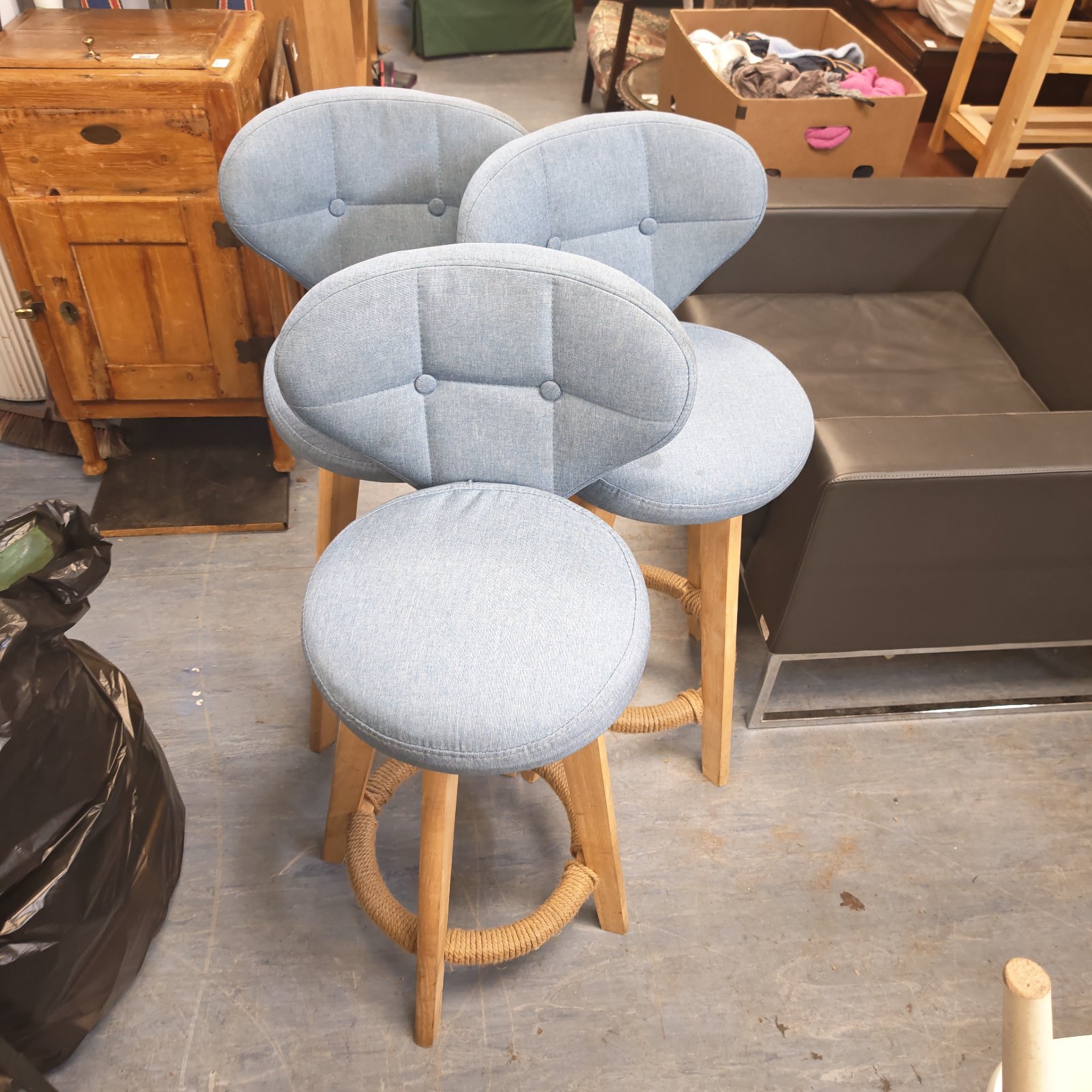 Three vintage wooden swivel bar stools with blue seats.