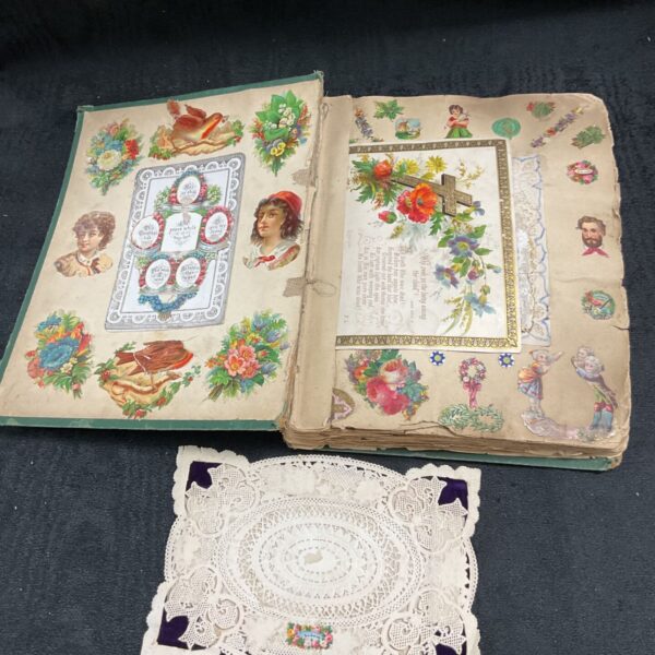 Open Victorian scrap album with colourful paper ephemera and lace doily.
