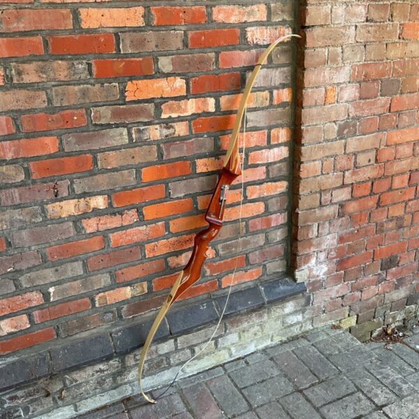 Vintage Forest Knight archery bow leaning against a brick wall.