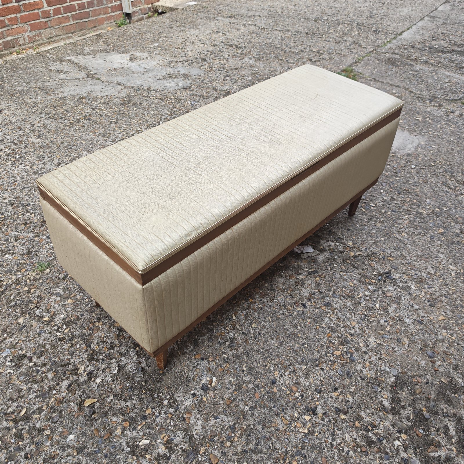 Vintage beige ottoman with dark brown trim, mid century style.