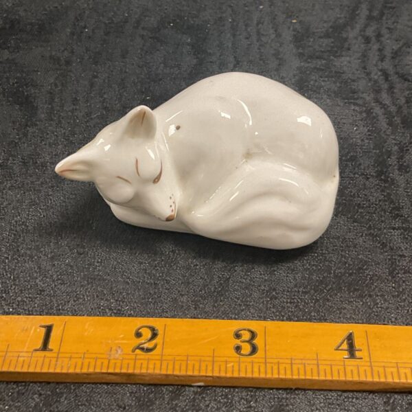 Vintage white ceramic cat figurine displayed with a ruler.