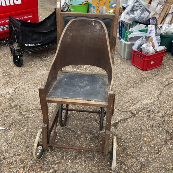 Vintage wooden child’s wheelchair with spoked wheels.