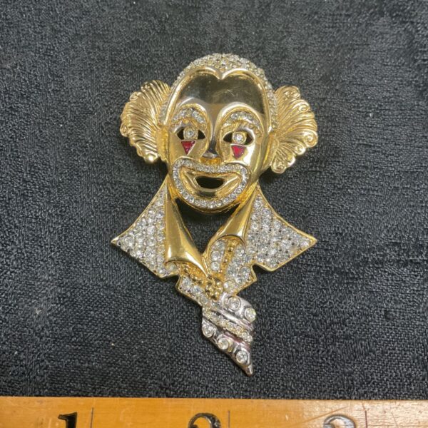 Close-up of vintage clown brooch with rhinestones and gold tone finish.