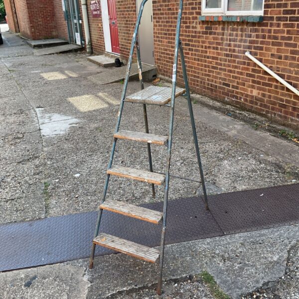 Vintage metal step ladder with wooden steps in a garden setting.