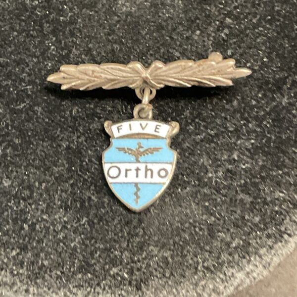 Vintage silver brooch with "Ortho" enamel shield and "FIVE" detail.