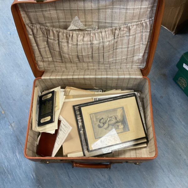 Vintage brown suitcase open with mixed ephemera inside.