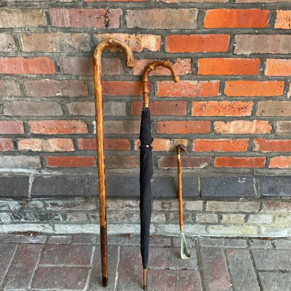 Vintage umbrella and carved walking sticks against a brick wall.