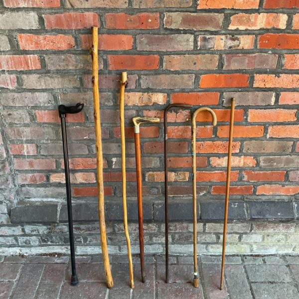 Lot of seven vintage walking sticks displayed against a brick wall.
