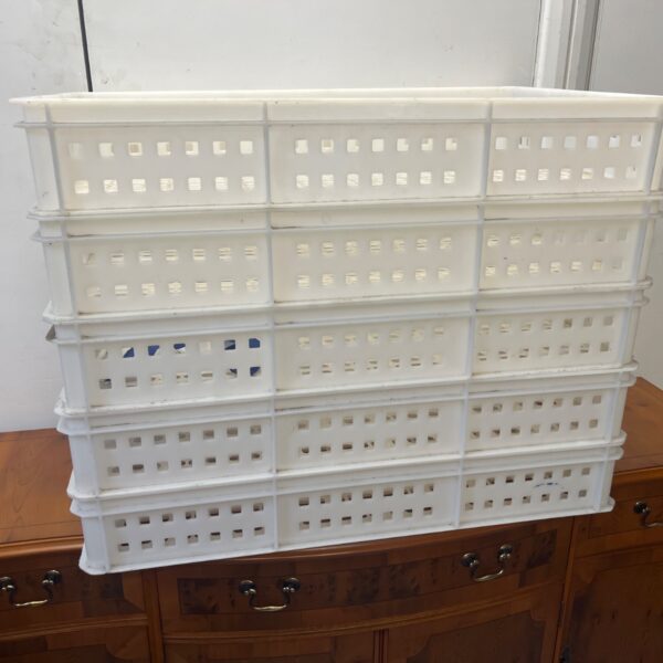 Five white plastic storage trays stacked on a wooden surface.