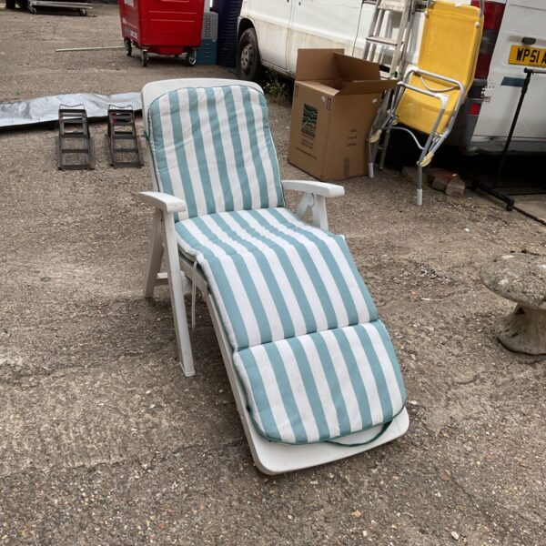 White plastic sun lounger with striped cushion in a garden setting.