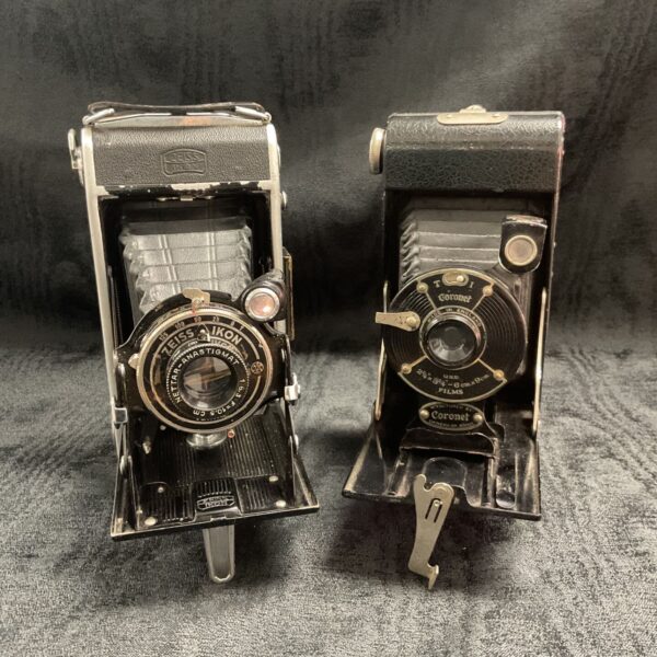 Two vintage bellows cameras, a Zeiss Ikon and Coronet, in a studio setting.