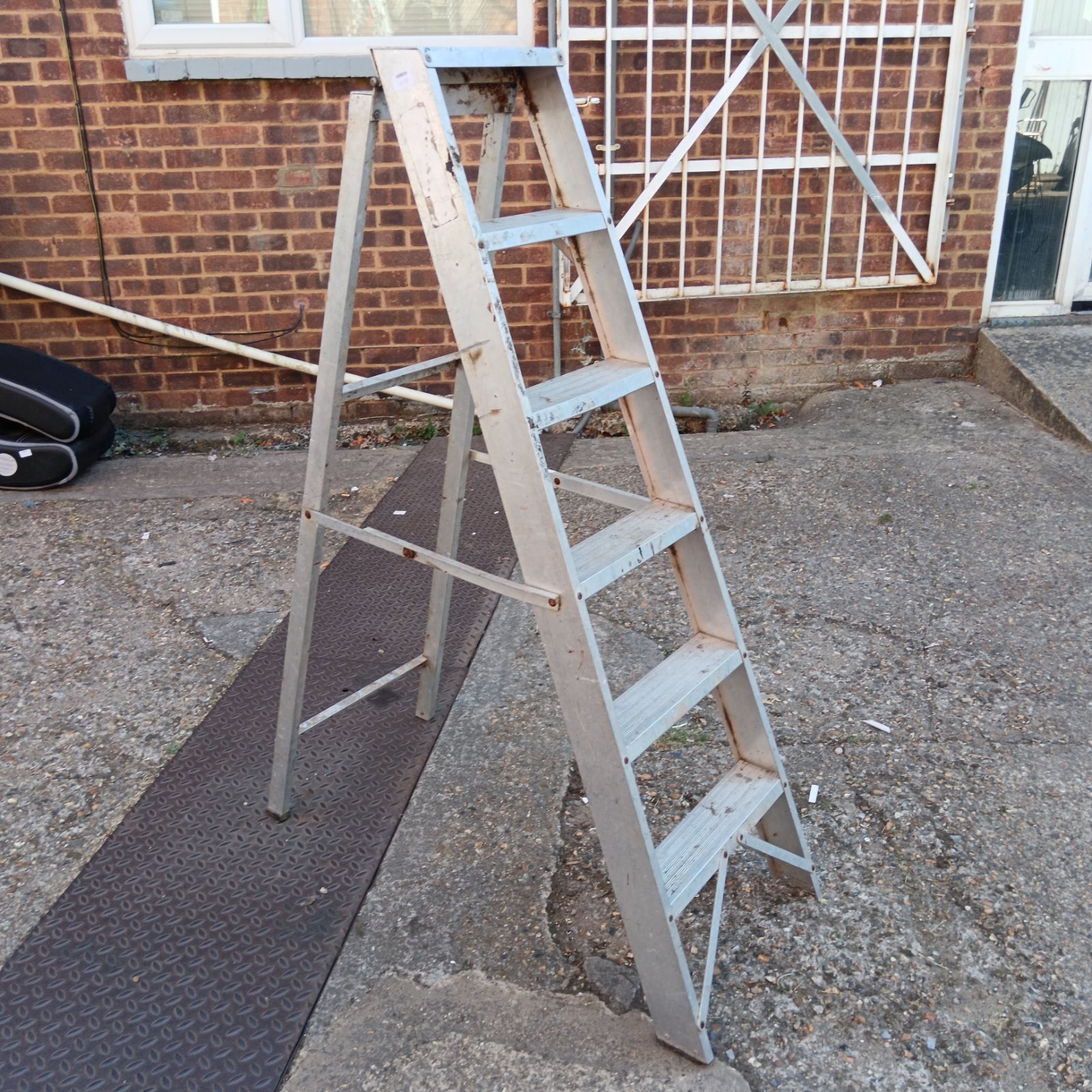 Aluminium six-rung step ladder against a brick wall.
