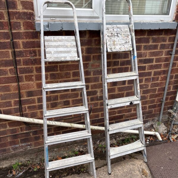 Pair of aluminium folding step ladders leaning against a wall.