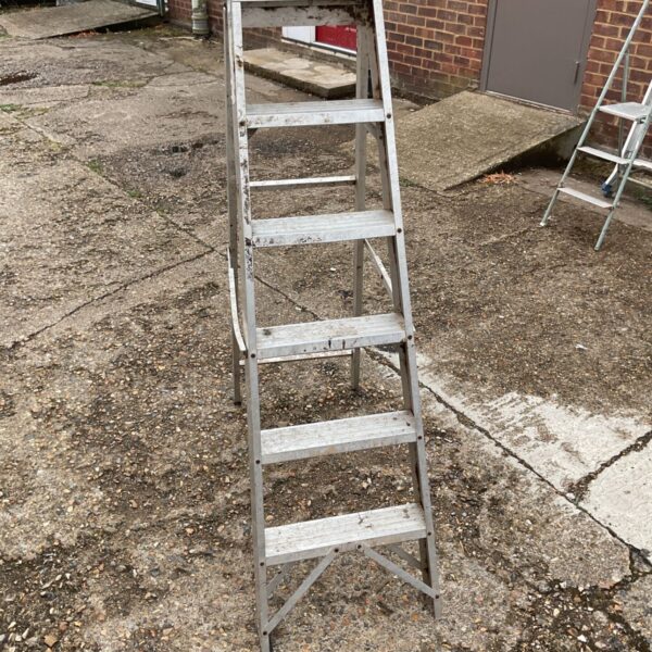 Aluminium swing-back step ladder with five treads, showing signs of wear.