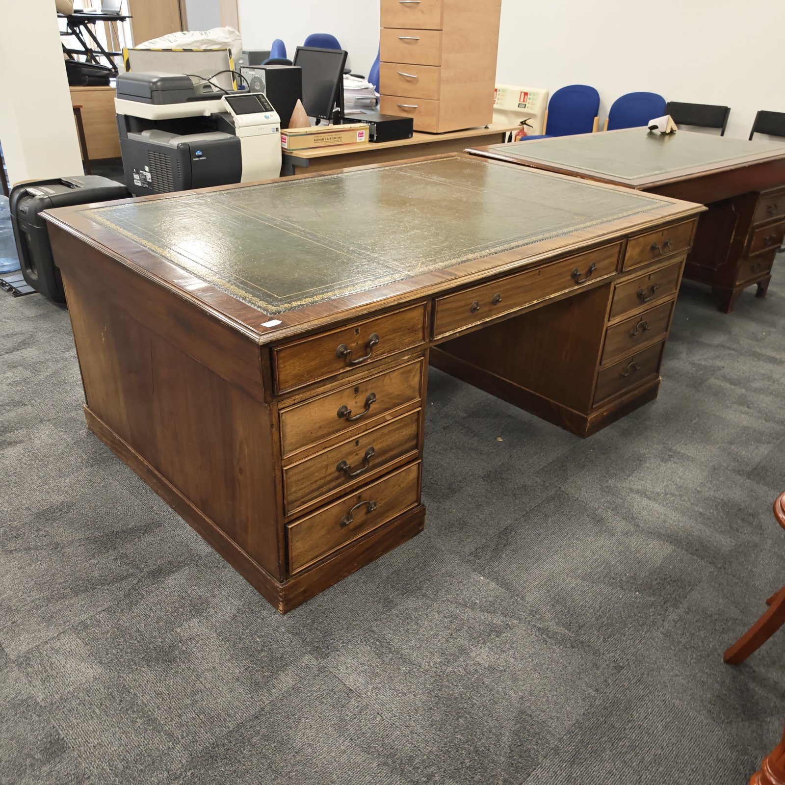 Antique mahogany partner's desk with green leather top in office setting.