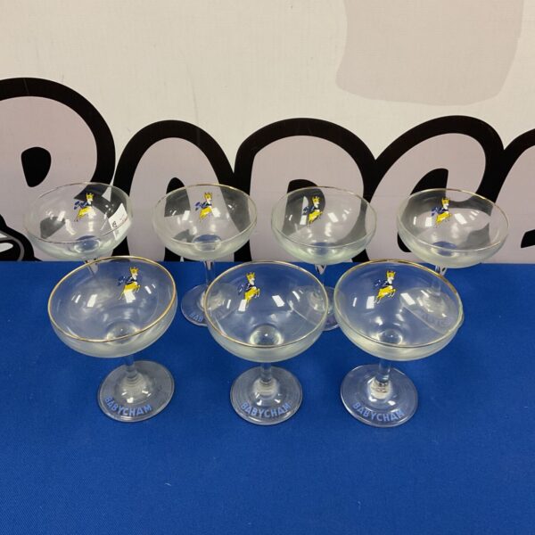 Set of seven vintage Babycham glasses on a white surface.