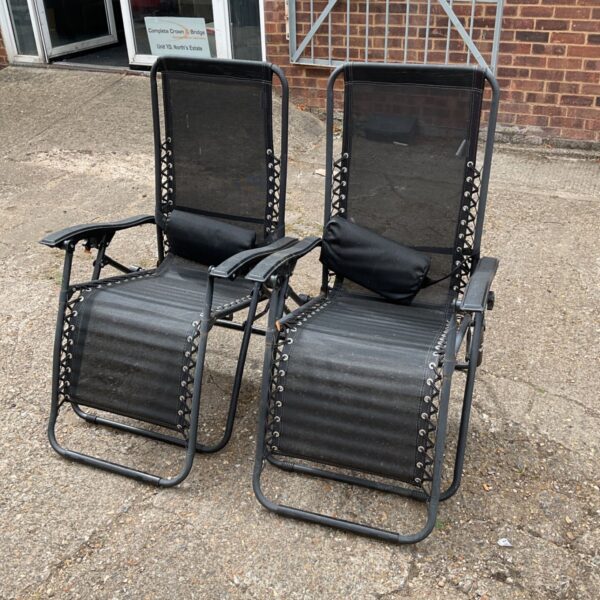 Pair of black recliner sun chairs in a garden setting.