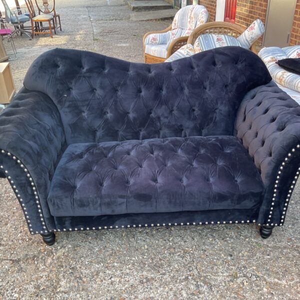 Black velvet tufted curved sofa with nailhead trim.