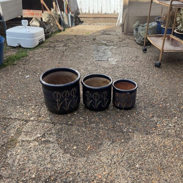 Set of three dark blue glazed ceramic plant pots for garden use.