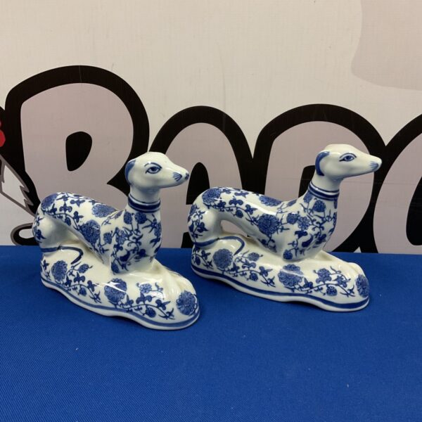 Vintage blue and white porcelain greyhound figurines on blue surface.