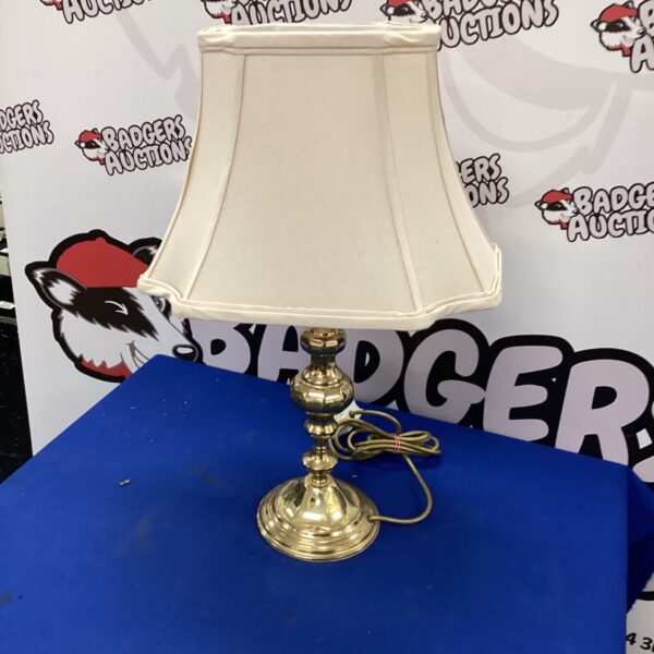 Vintage brass table lamp with a cream lampshade on a dark surface.