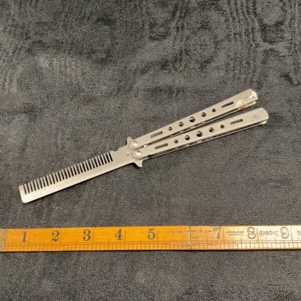 Stainless steel butterfly comb with teeth, shown against a dark background.