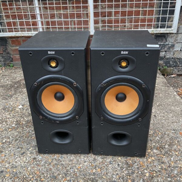 Pair of black B&W DM602 monitor speakers against a brick wall.