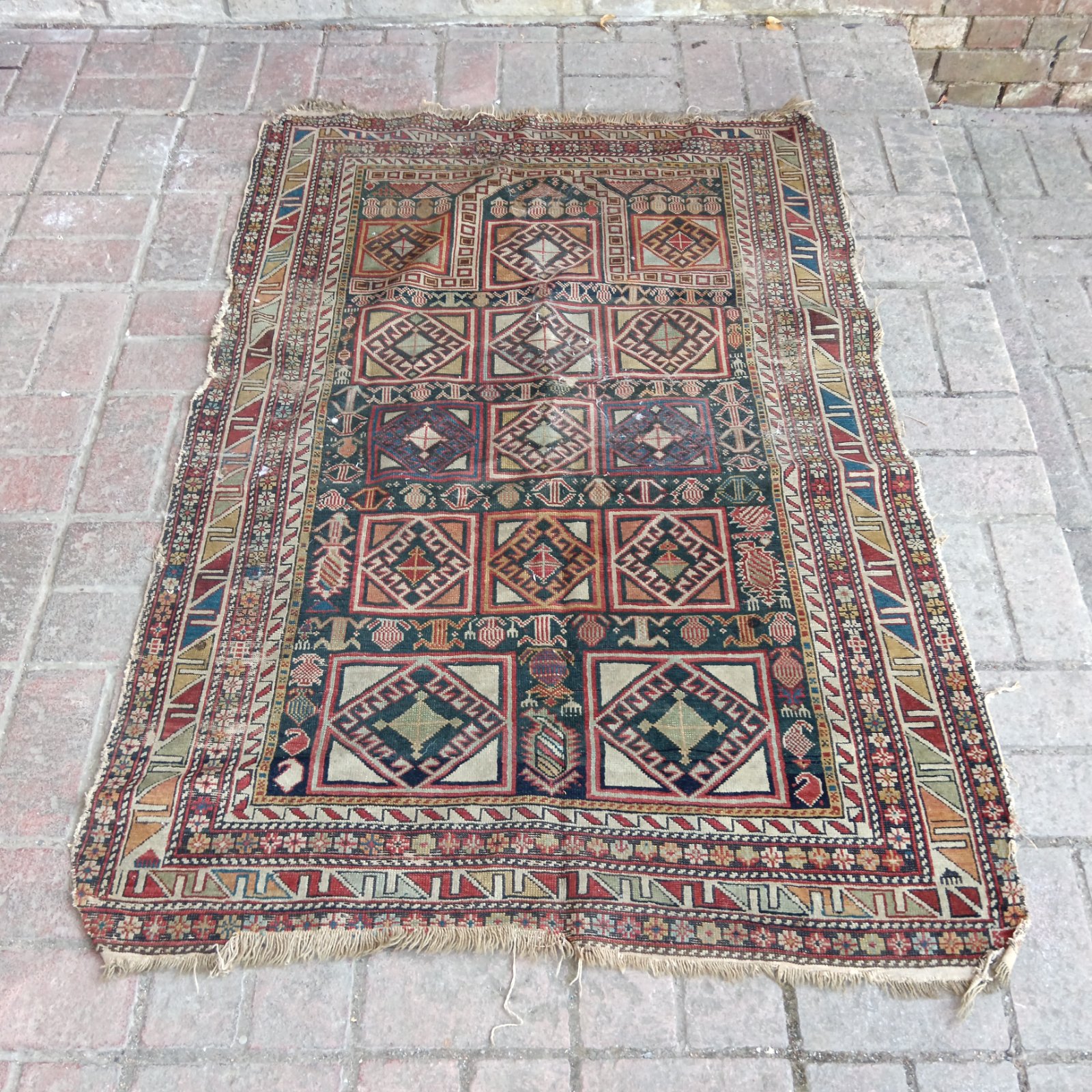 Antique Caucasian rug with vibrant geometric patterns and worn texture.