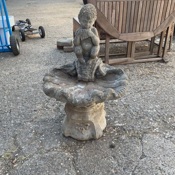 Vintage garden bird bath with cherub playing panpipes.