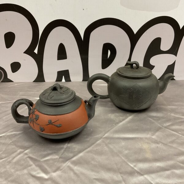 Pair of antique Chinese Yixing teapots on a textured surface.