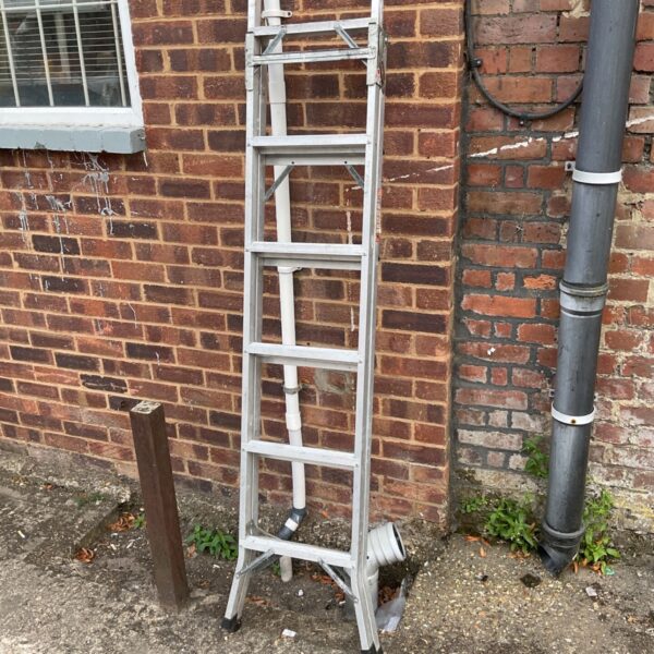 Aluminium combination ladder leaning against a brick wall.