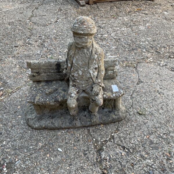 Vintage concrete garden statue of a man on a bench.