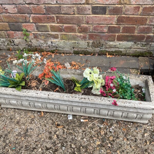 Grey concrete planter filled with colourful artificial flowers in a garden.