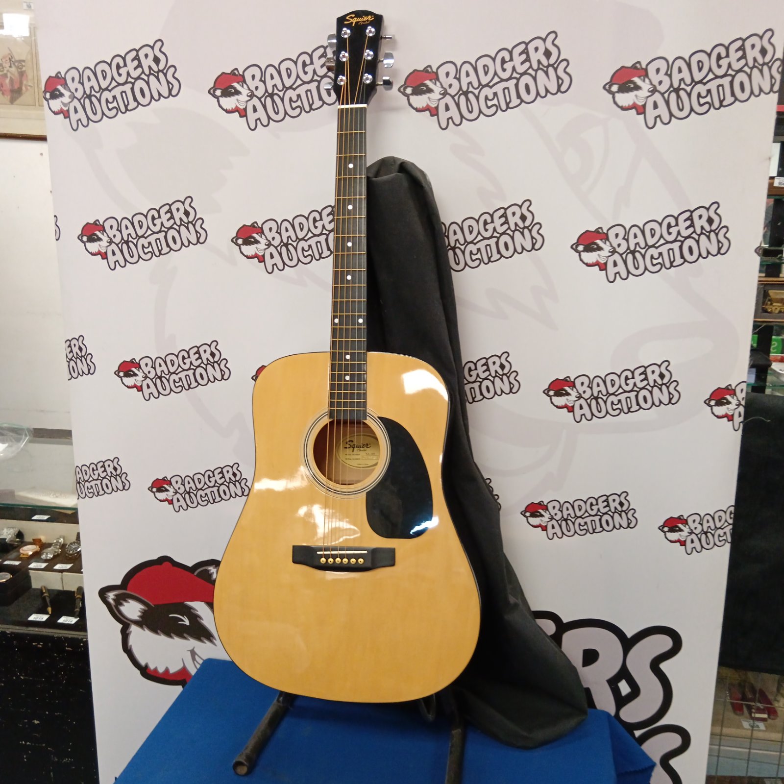 Fender Squire SA-105 acoustic guitar with case displayed against backdrop.
