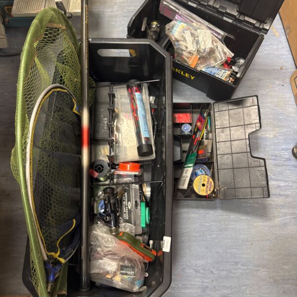 Overview of a fishing tackle lot with boxes, reels, and a landing net.