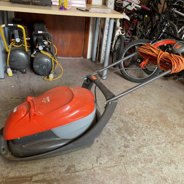 Orange and black Flymo Easy Glide 300 electric lawnmower in a garage.