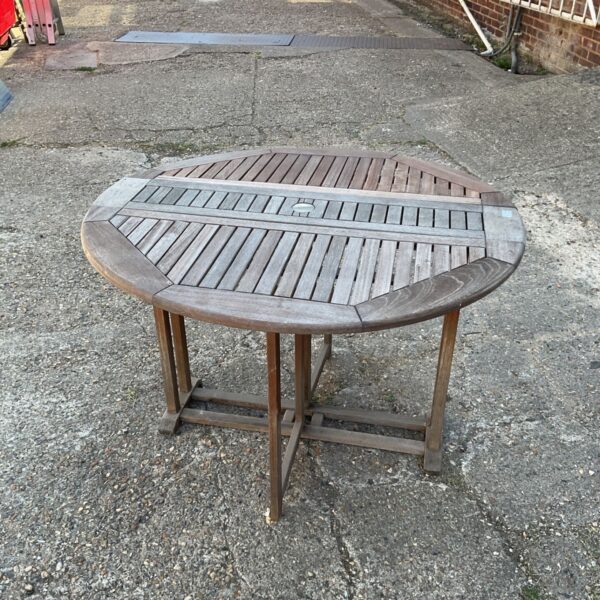 Weathered folding teak garden table in a gravel yard.