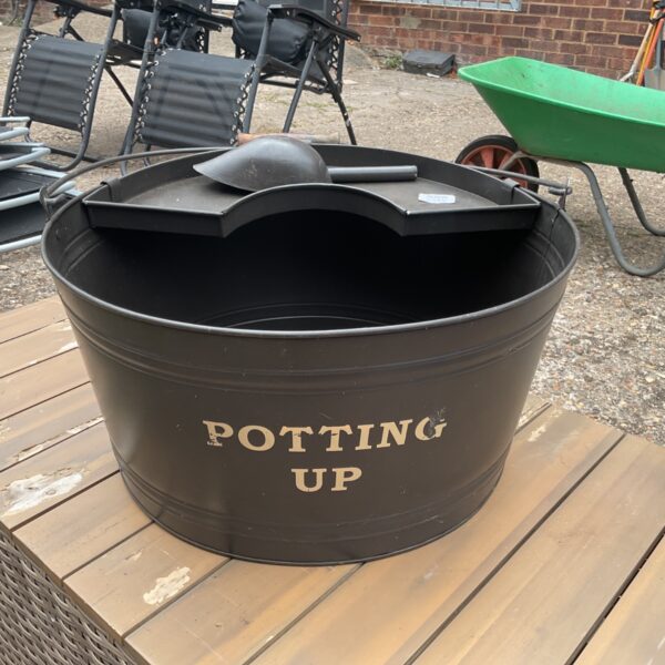 Black metal garden potting bench with integrated shelf and shovel.