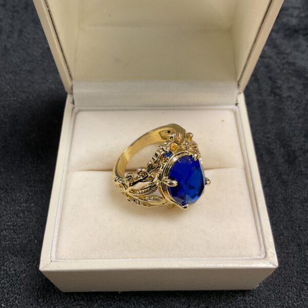 Gold tone ring with a blue CZ and foliate design.