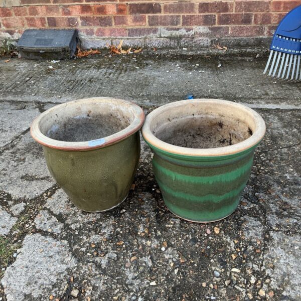 Two green glazed terracotta garden pots in a garden setting.
