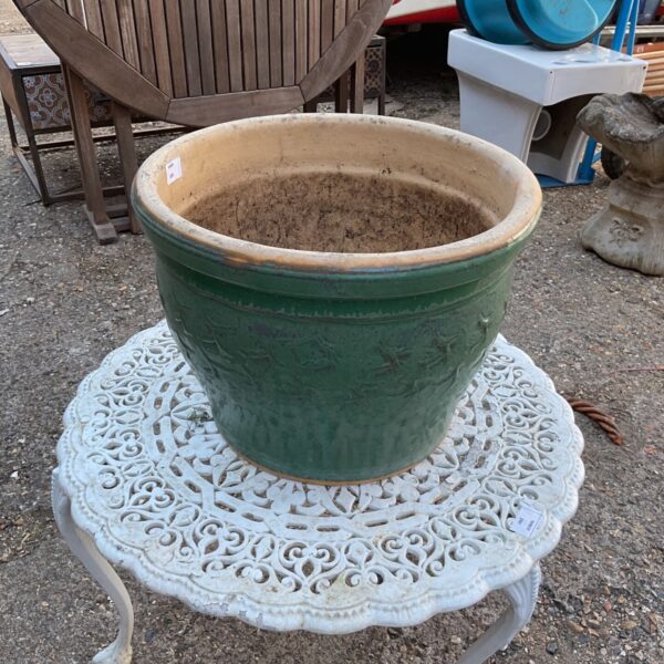 Green glazed terracotta plant pot in a garden setting.