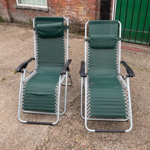 Two green recliner deck chairs in a garden setting.