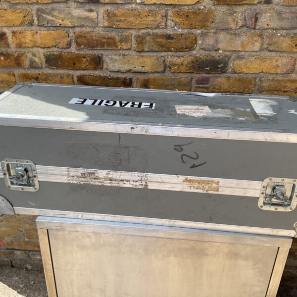 Grey industrial flight case leaning against a brick wall.