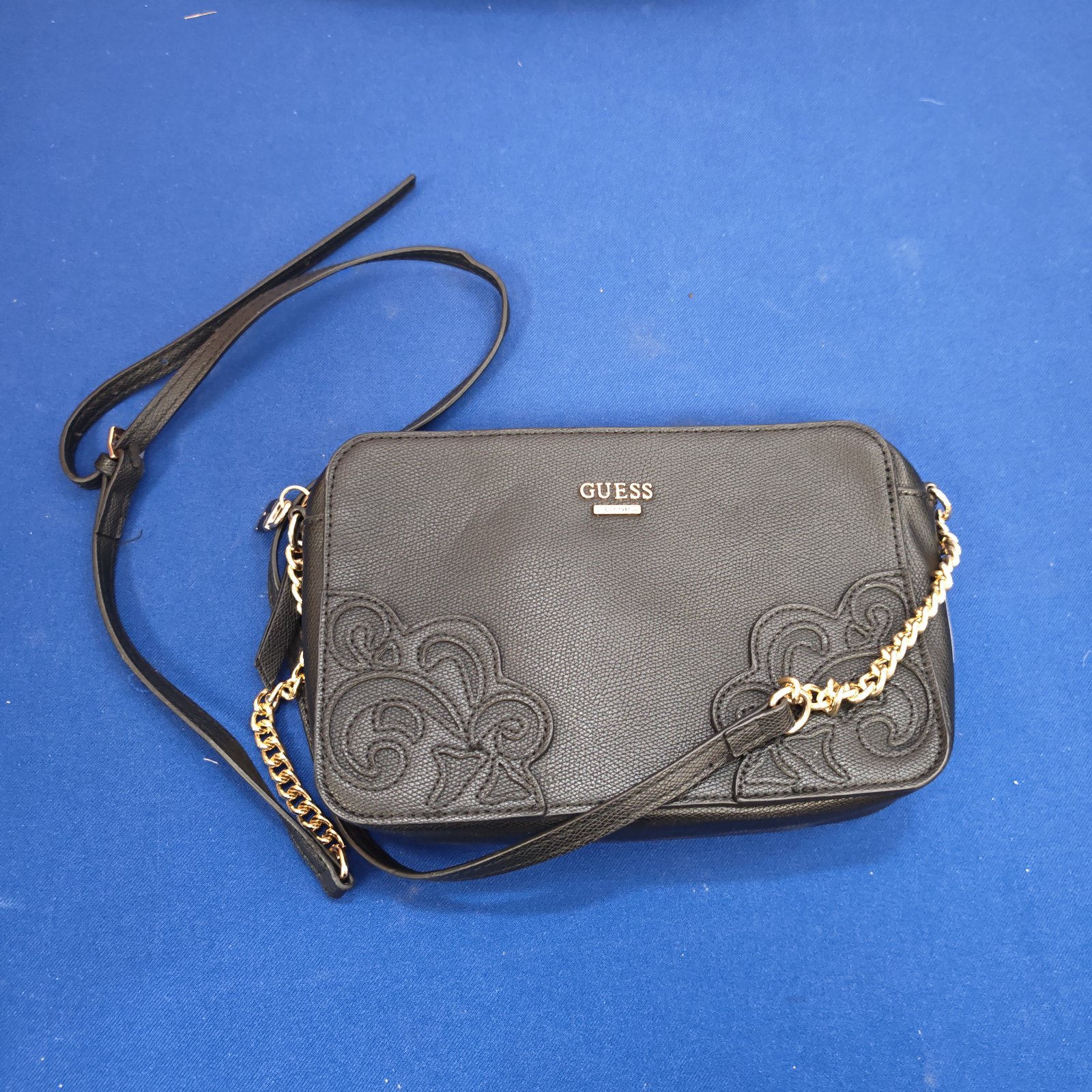 Black Guess handbag with embossed floral pattern and gold chain strap.