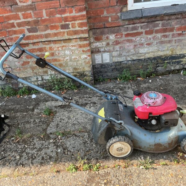 Side view of a vintage Honda petrol lawn mower in a garden.