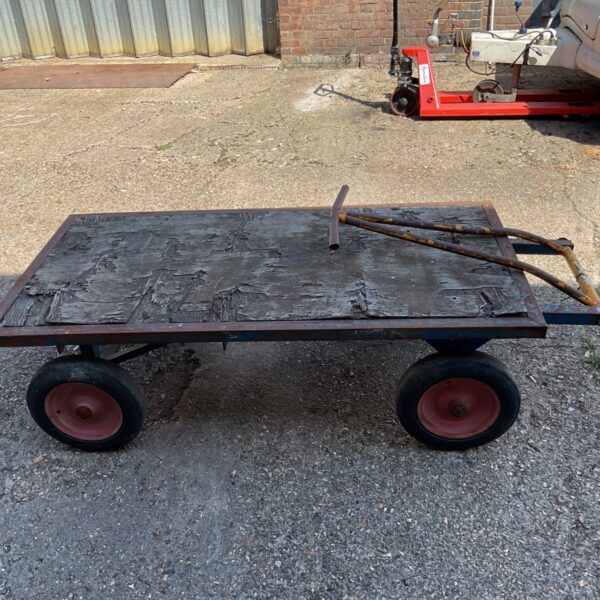 Heavy-duty industrial flatbed trolley with wooden deck and four wheels.