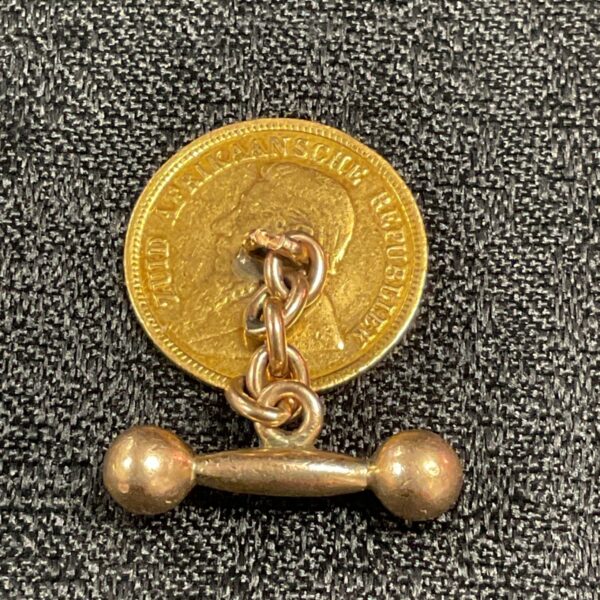 Antique Kruger Half Pond gold cufflink on textured background.