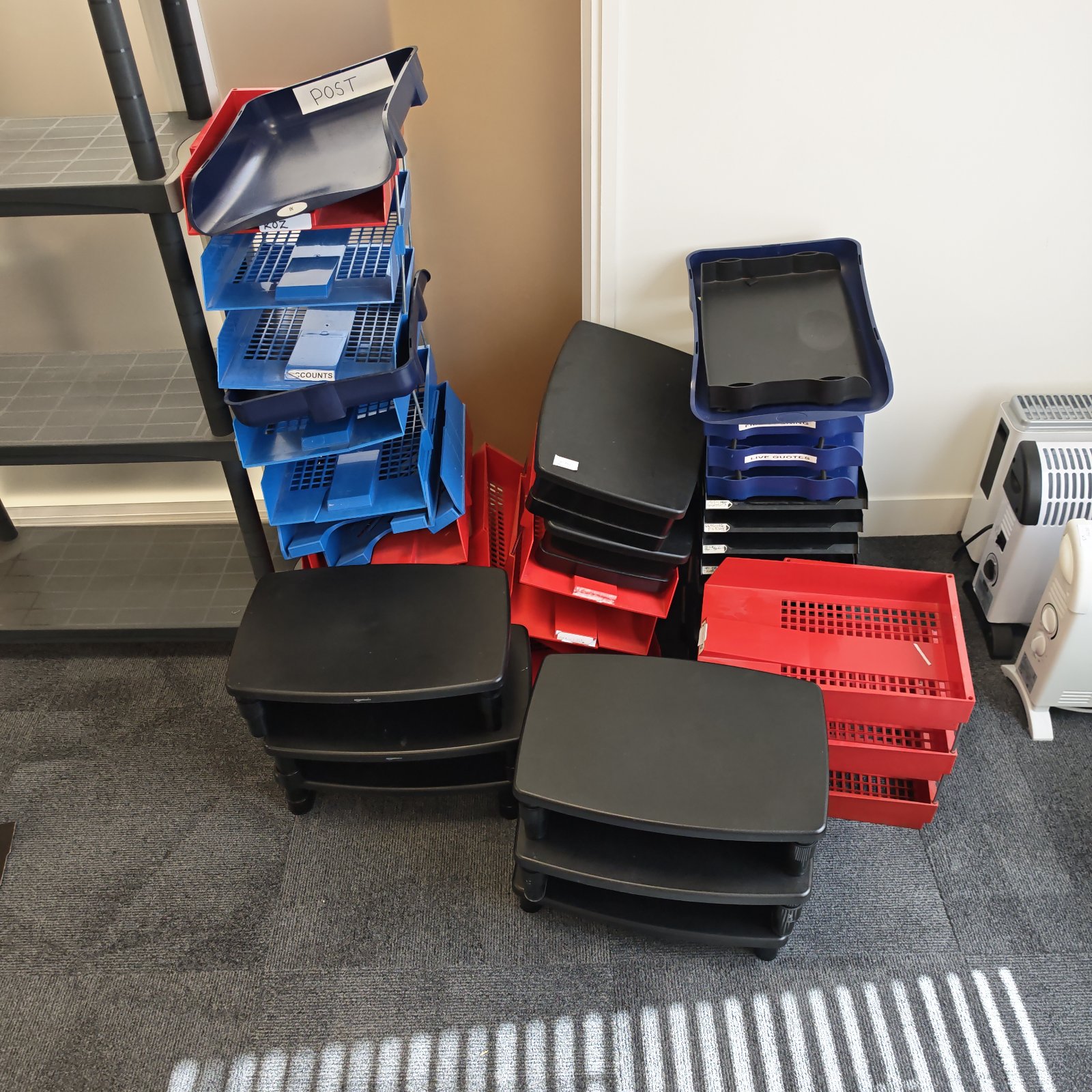 Colourful letter trays stacked with black monitor riser on desk.