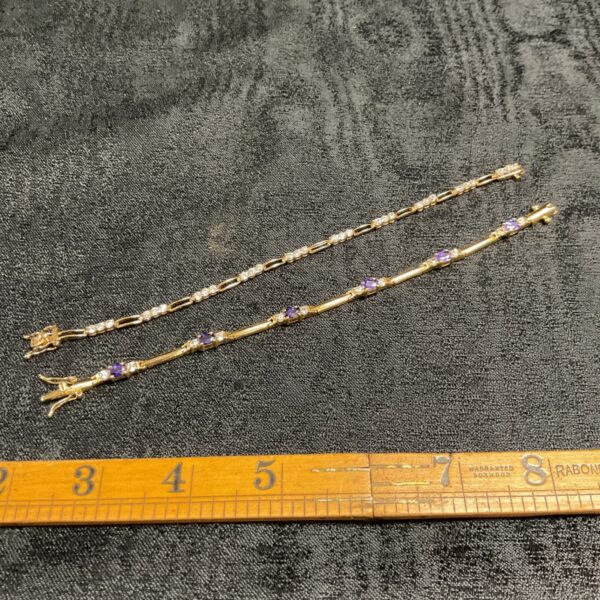 two gilt bracelets one with white stones and one with oval amethyst colour stones