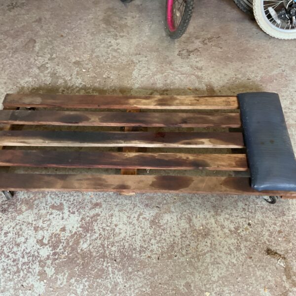 Low-profile mechanic's creeper with wooden frame and vinyl cushion.